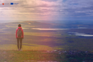 Woman standing at the top of a hill with fenomenal views, Lapland, Finland. Logos of Lapin liitto and EU co-funded.