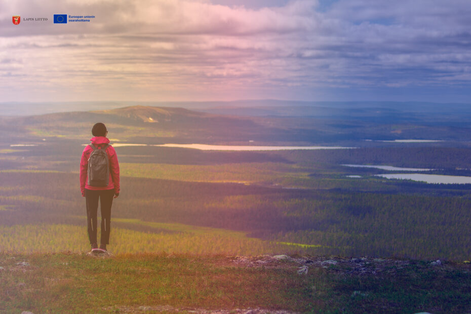 Woman standing at the top of a hill with fenomenal views, Lapland, Finland. Logos of Lapin liitto and EU co-funded.